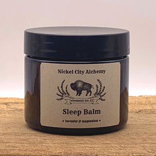 A dark amber glass jar of Nickel City Alchemy Sleep Balm