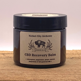 A jar of Nickel City Alchemy CBD Recovery Balm with a label indicating it contains CBD and magnesium, and is vegan, organic, and cruelty-free.